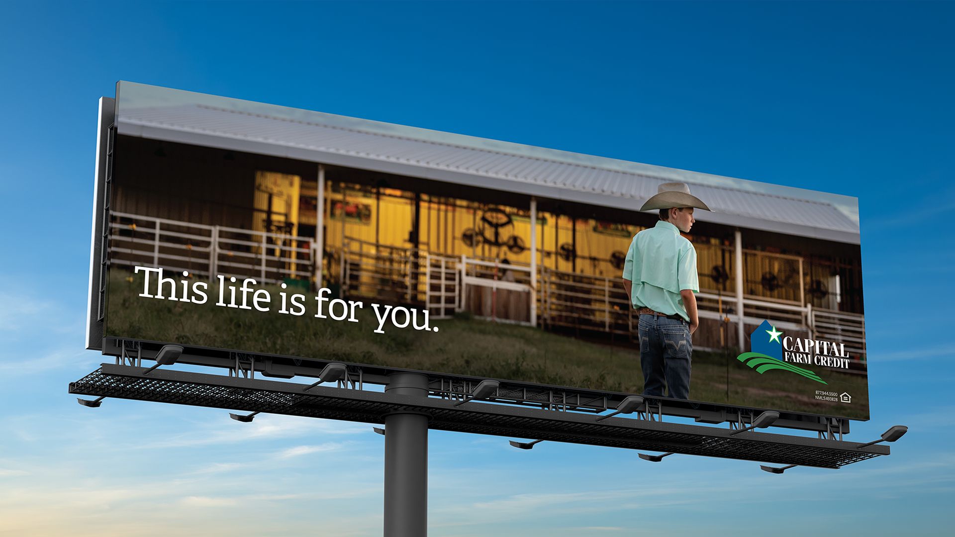 Capital Farm Credit billboard: person in cowboy hat looking toward a lit barn at dusk, text reads This life is for you.