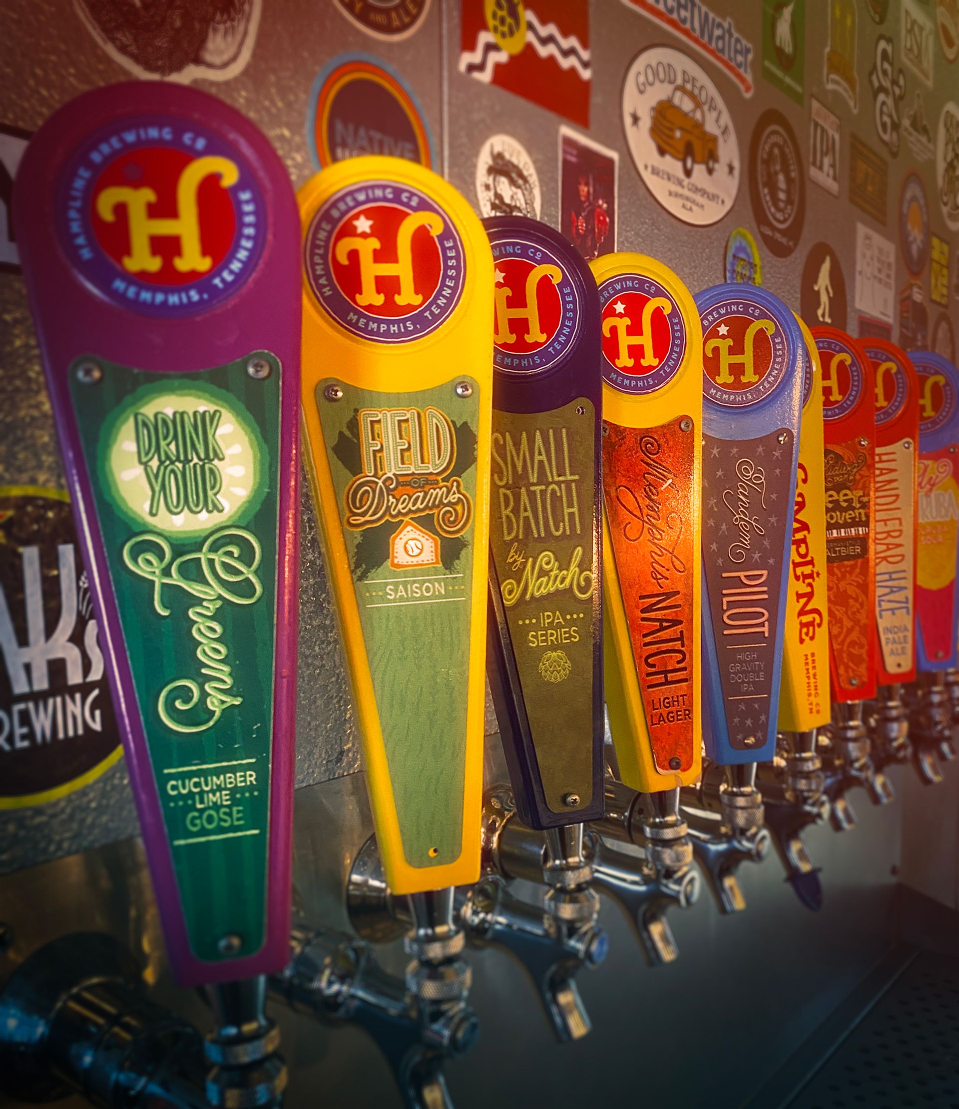 Row of colorful Hampline Brewing Co. beer tap handles in a brewery.