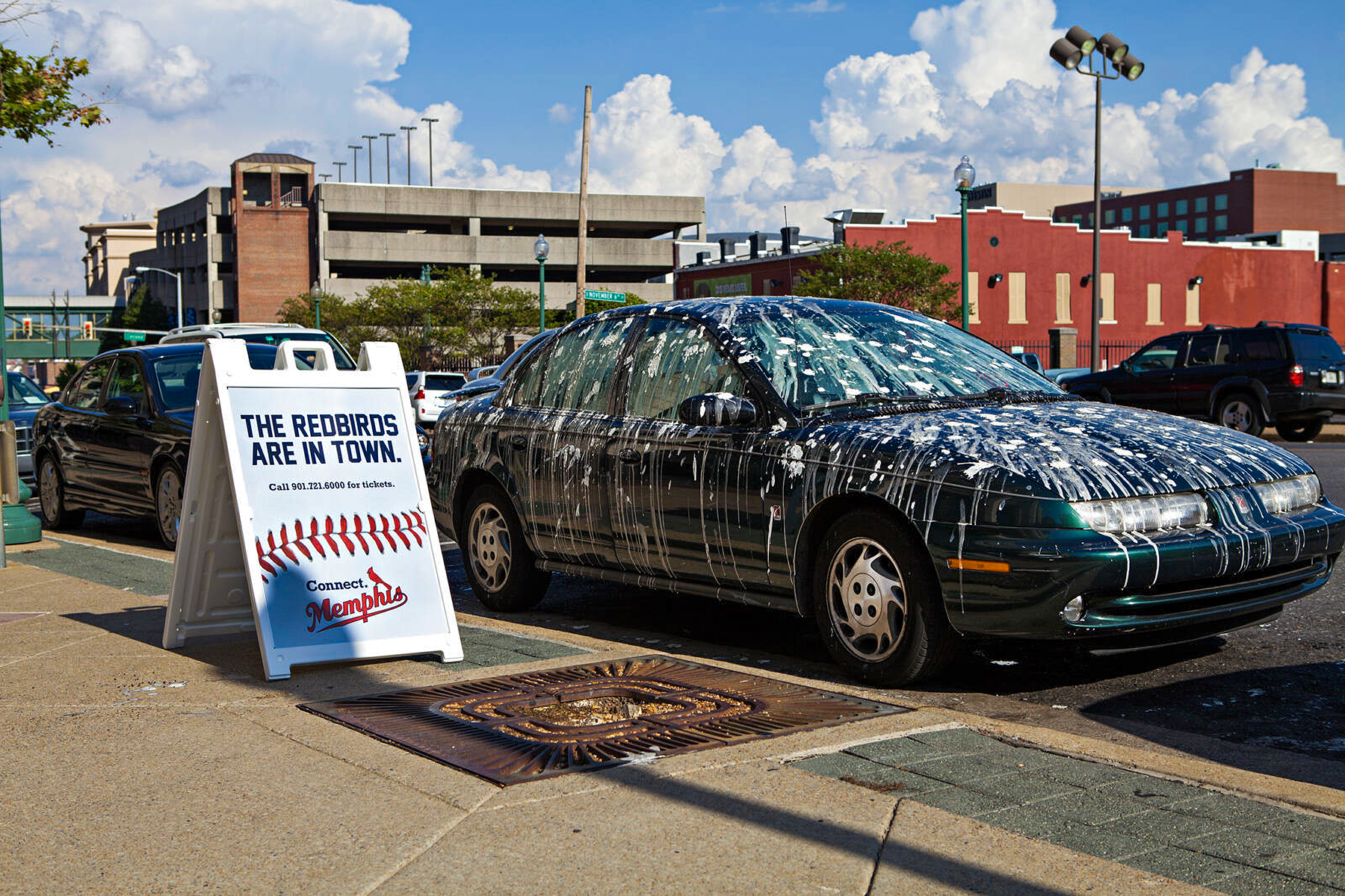 Outdoor activation featuring an A-frame sign reading "The Redbirds Are In Town" beside a car covered in simulated bird droppings, staged on a downtown Memphis sidewalk.