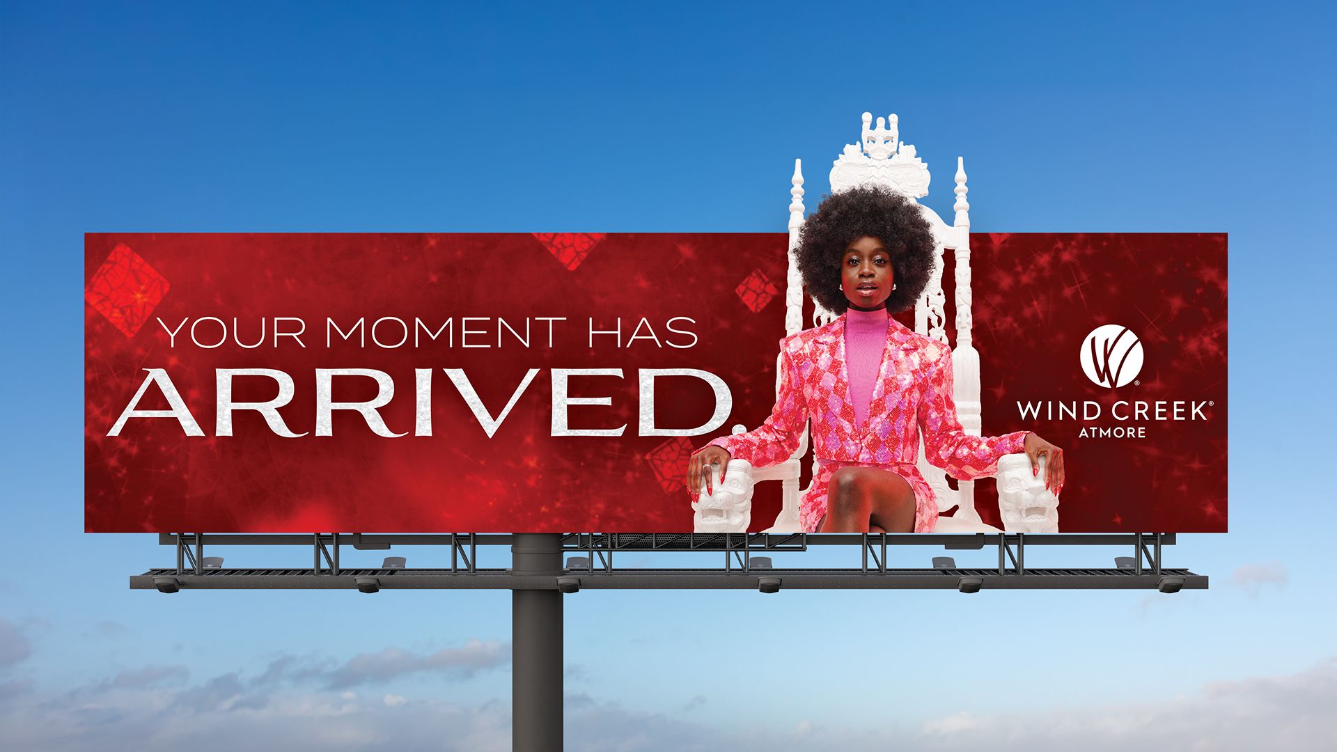 Billboard advertising Wind Creek Atmore with a woman sitting on a white ornate chair, surrounded by text 'YOUR MOMENT HAS ARRIVED.' and red diamond graphics.
